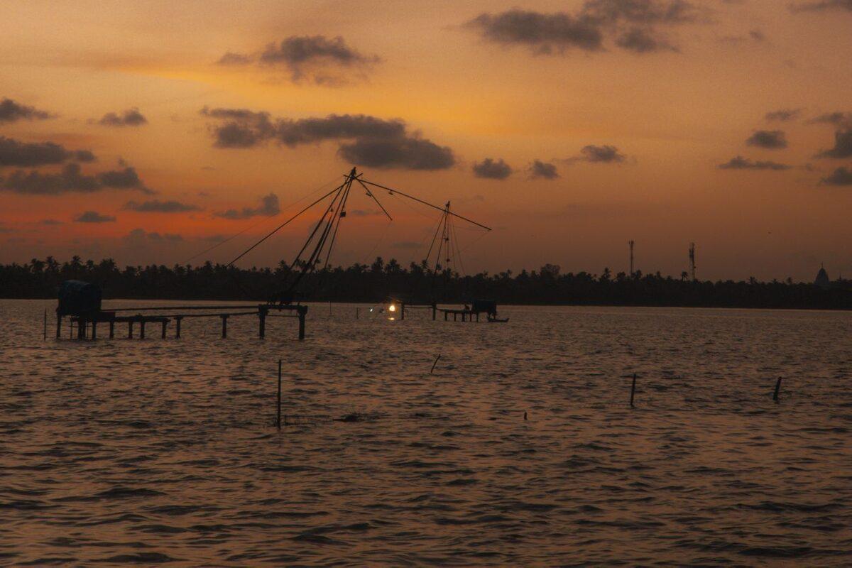 Cantilevered Chinese fishing nets silhouetted against a sunset over the water at Fort Kochi