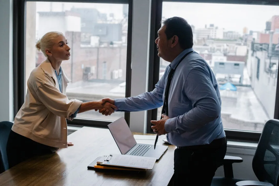 Two colleagues shaking hands across an office desk